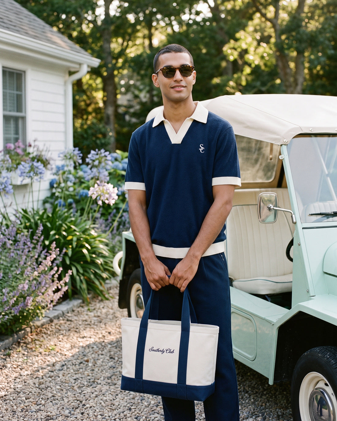 Campaign concept: man wearing a navy polo and holding a cream and navy Southerly tote. Garment details and fit are unconfirmed.