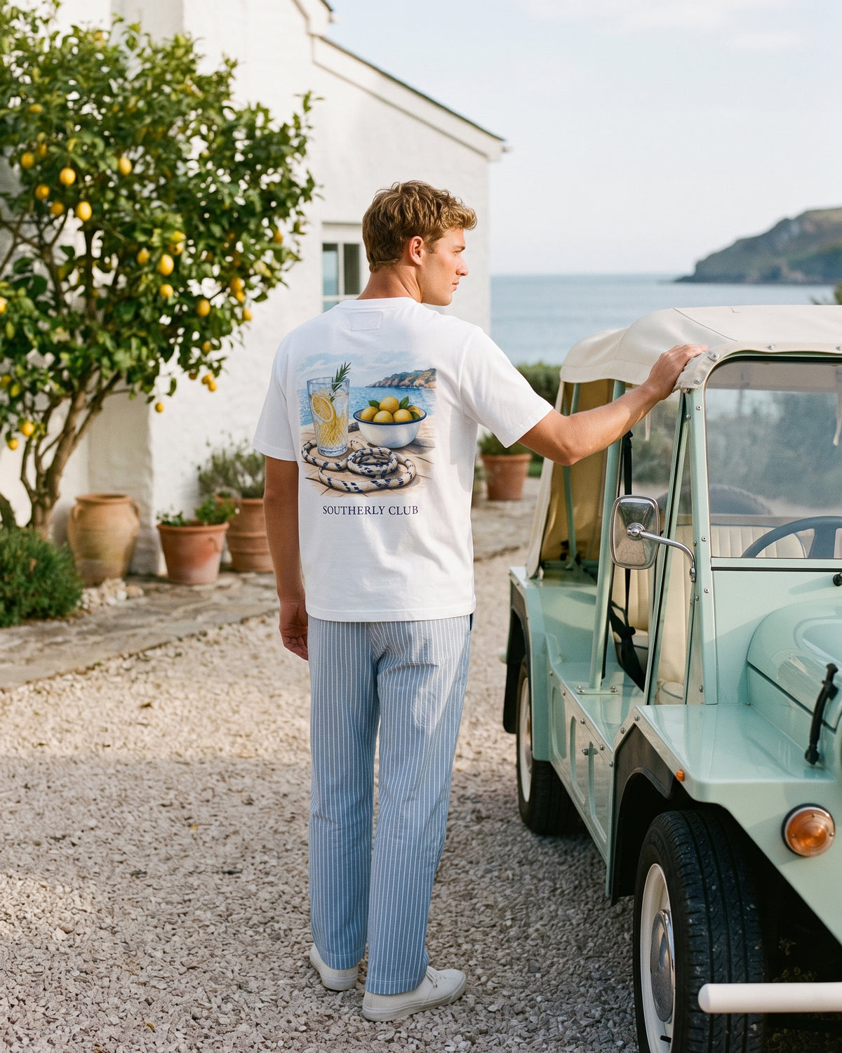 Campaign concept: man wearing a white citrus graphic tee beside a mint car and lemon tree. Garment details and fit are unconfirmed.