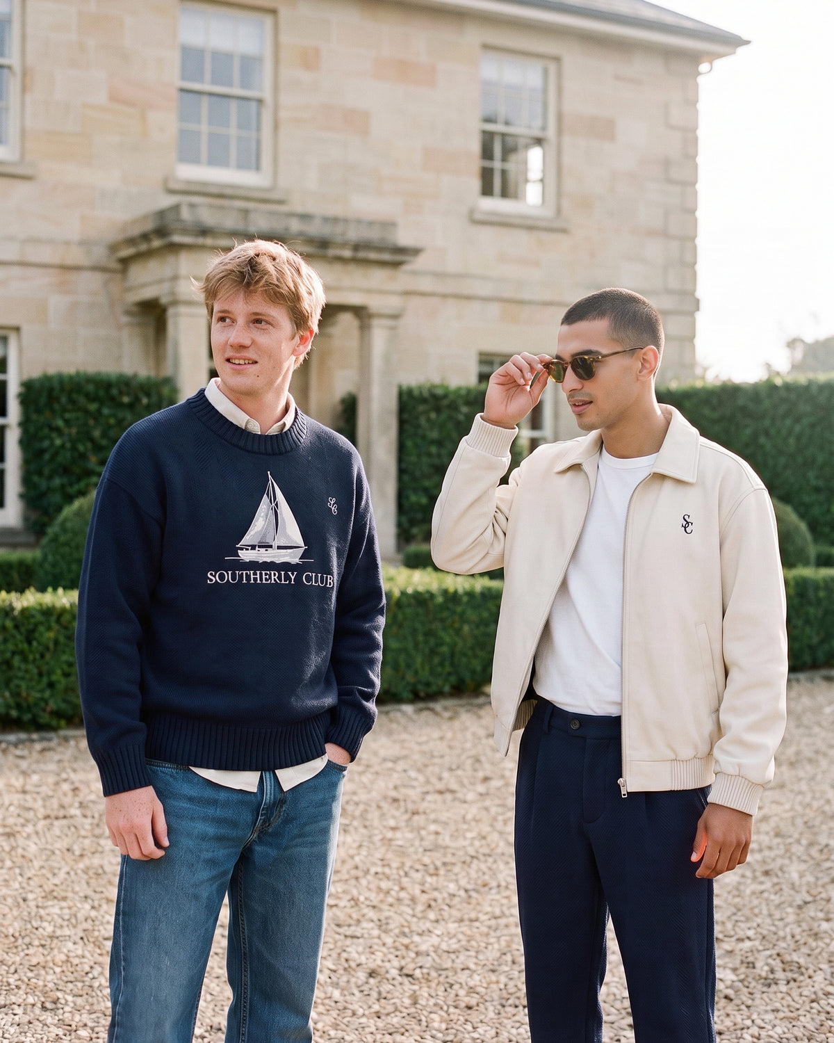 Campaign concept: two men wearing a navy sailboat jumper and cream jacket. Garment details and fit are unconfirmed.