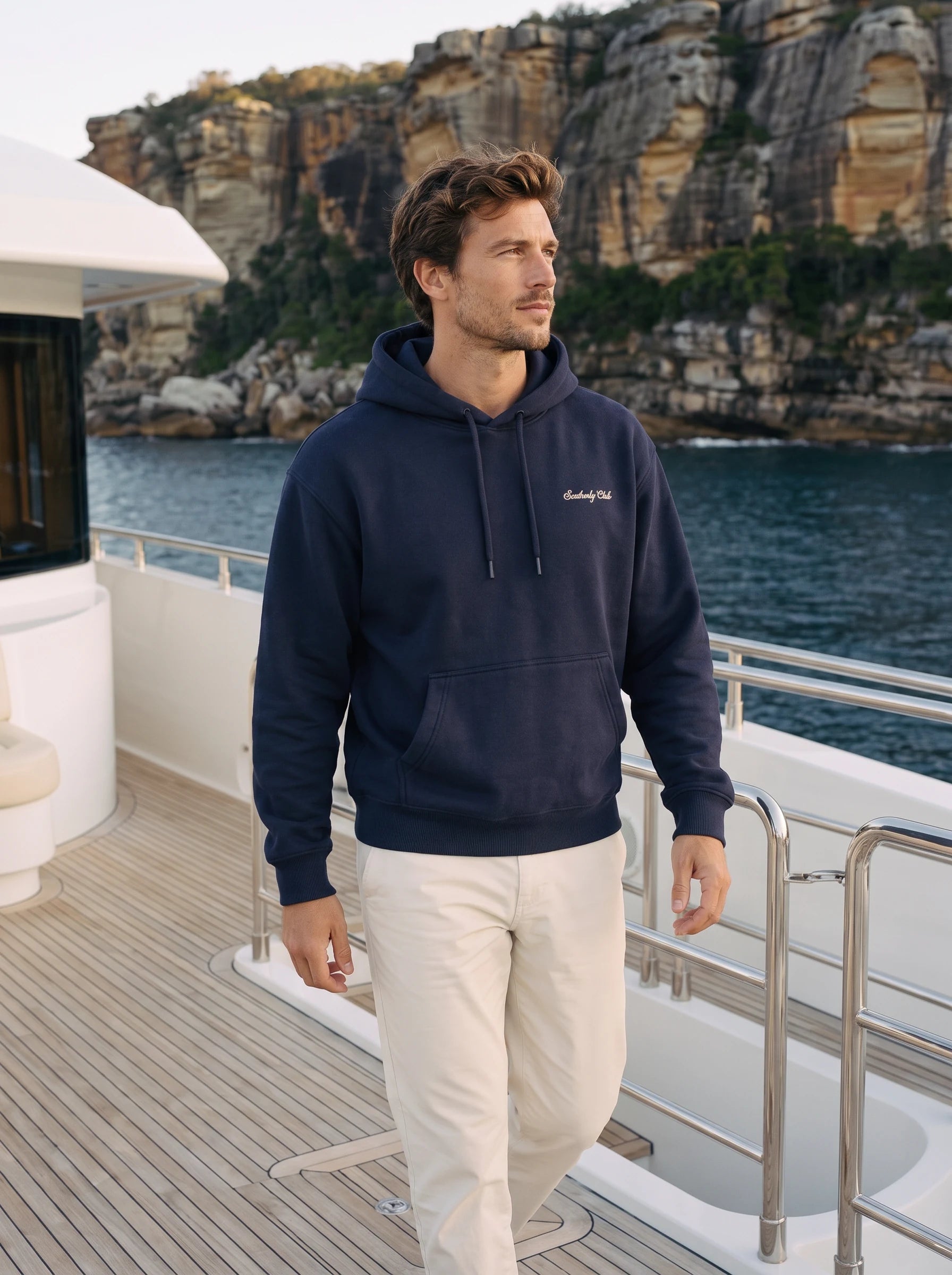 AI-generated campaign concept: an adult model in the navy Club hoodie on a white yacht deck. Garment fit unconfirmed.